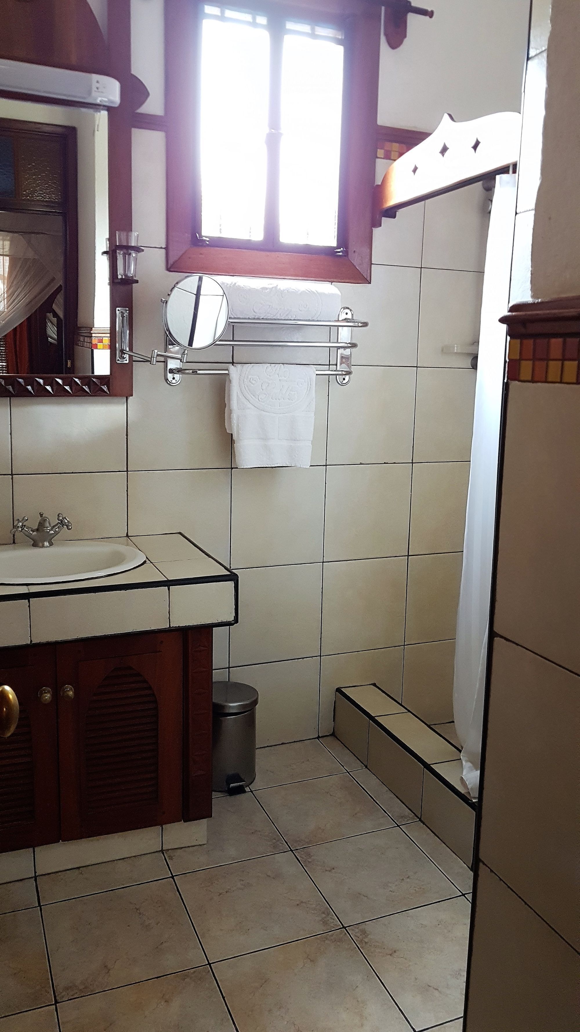 Une salle de bain comprenant un lavabo, un miroir, une fenêtre, un porte-serviettes et un espace douche.