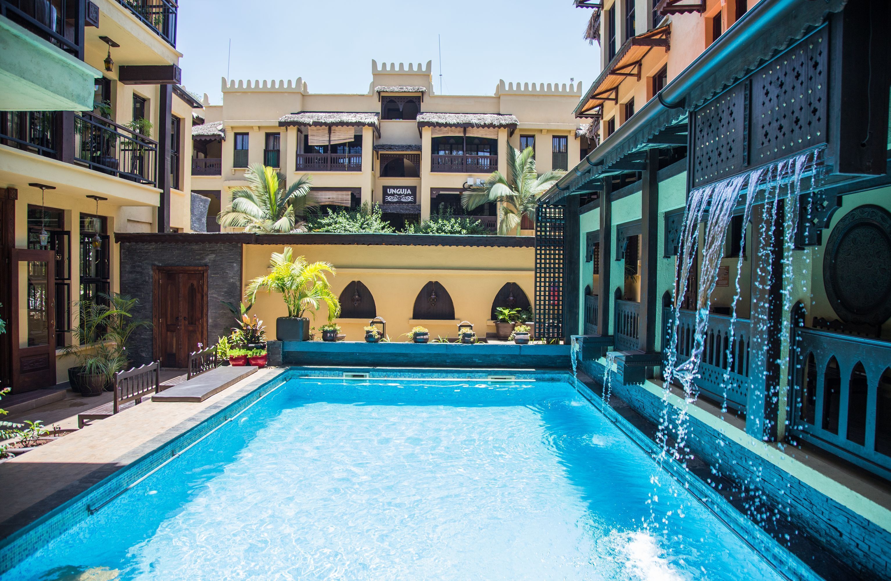 A swimming pool with a water feature, surrounded by buildings with balconies and a sign that reads "UNQUIA".