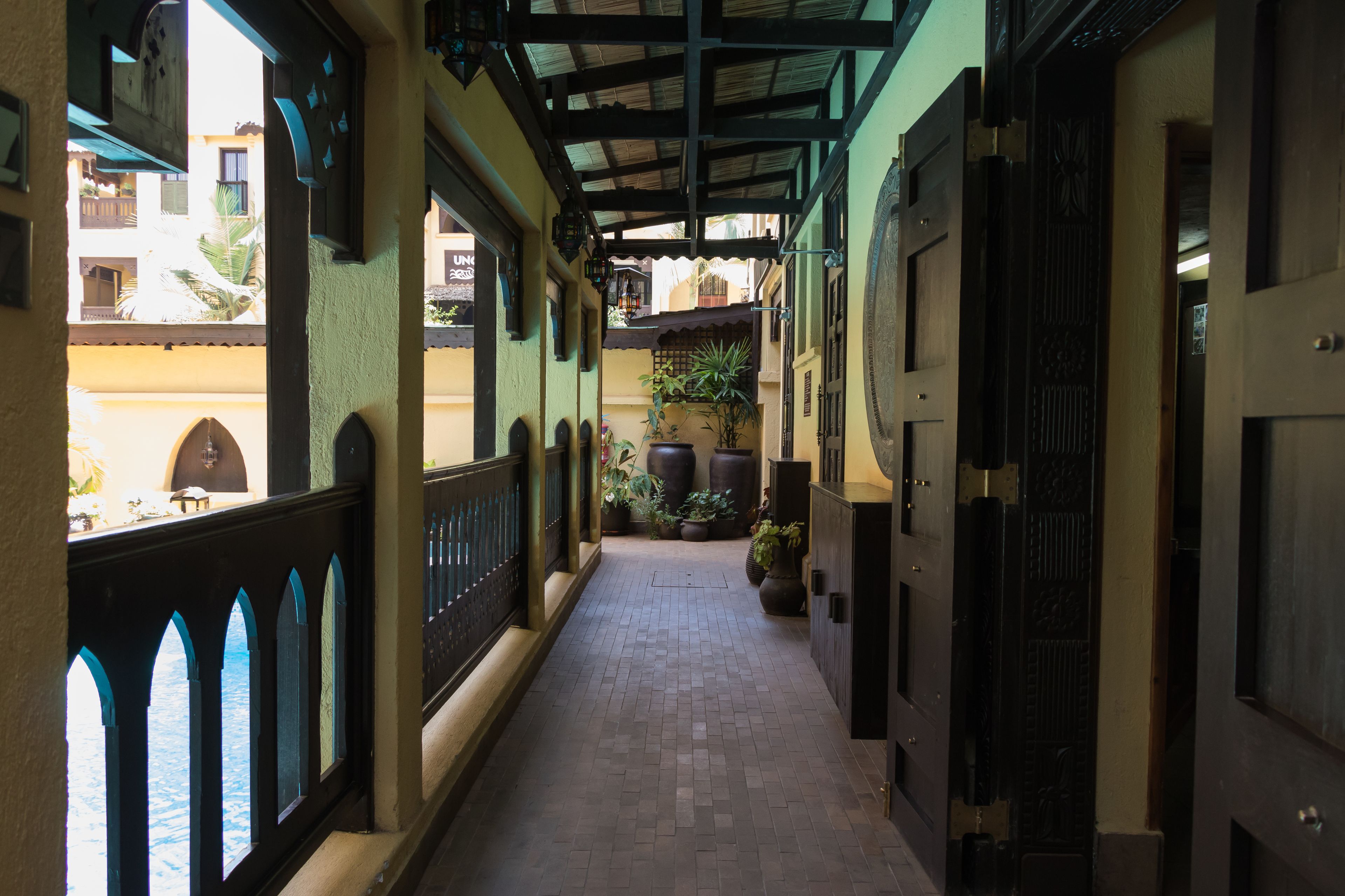 A corridor with a tiled floor, a railing on one side, and potted plants along the path.