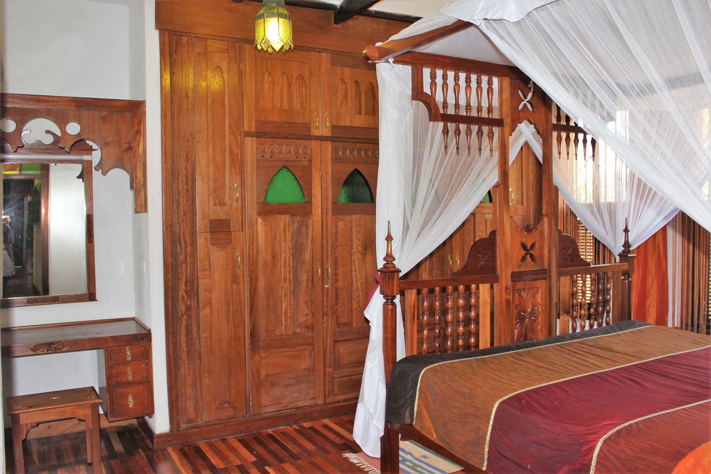A traditional wooden room with a bed, a mirror, and a wooden wardrobe.