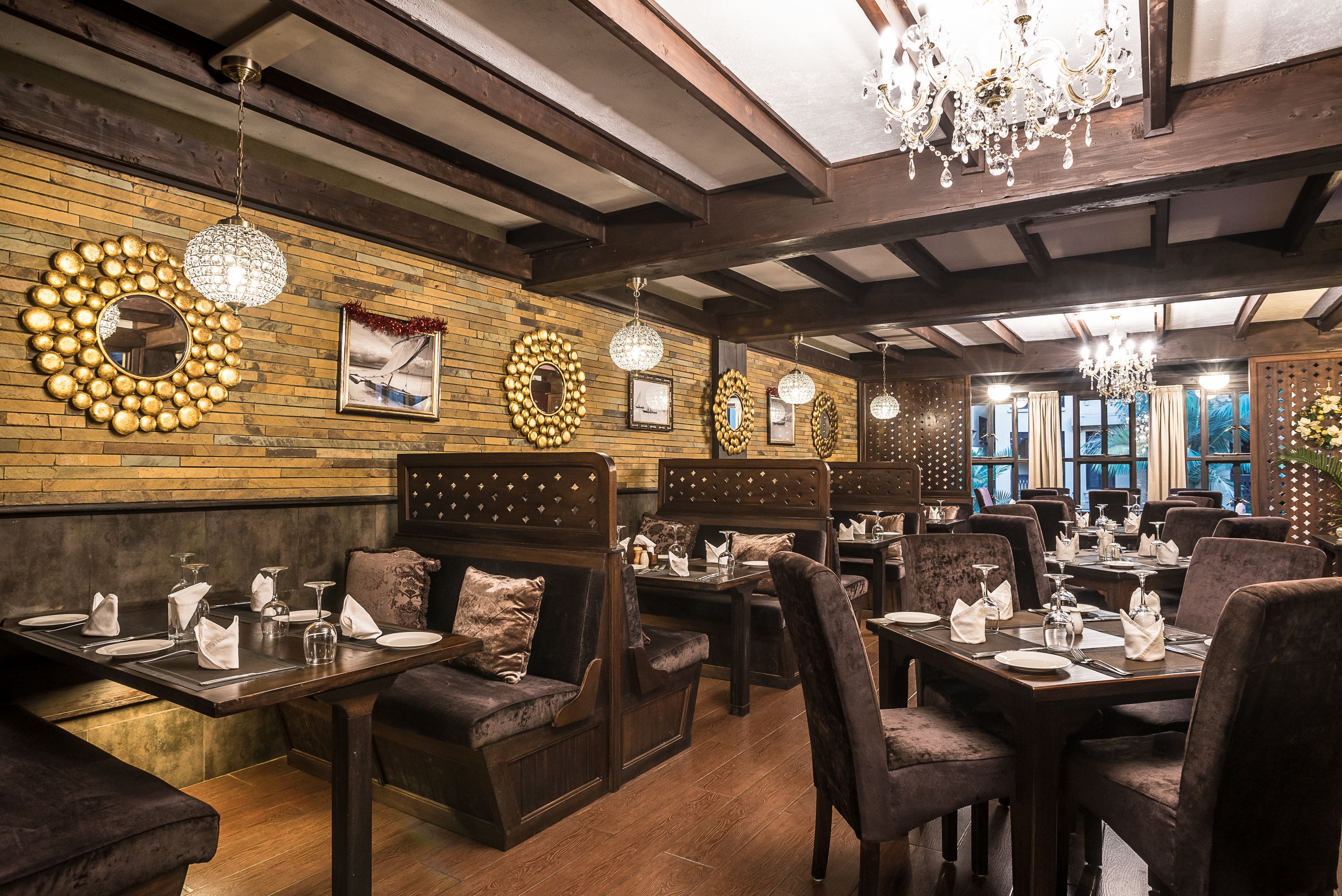 A restaurant with wooden walls, chandeliers, and neatly set dining tables.