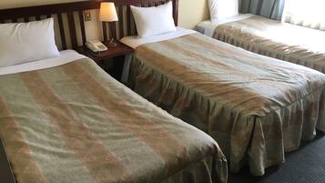 Una habitación de hotel con dos camas, cada una con cabecero, mesita de noche con lámpara y teléfono.