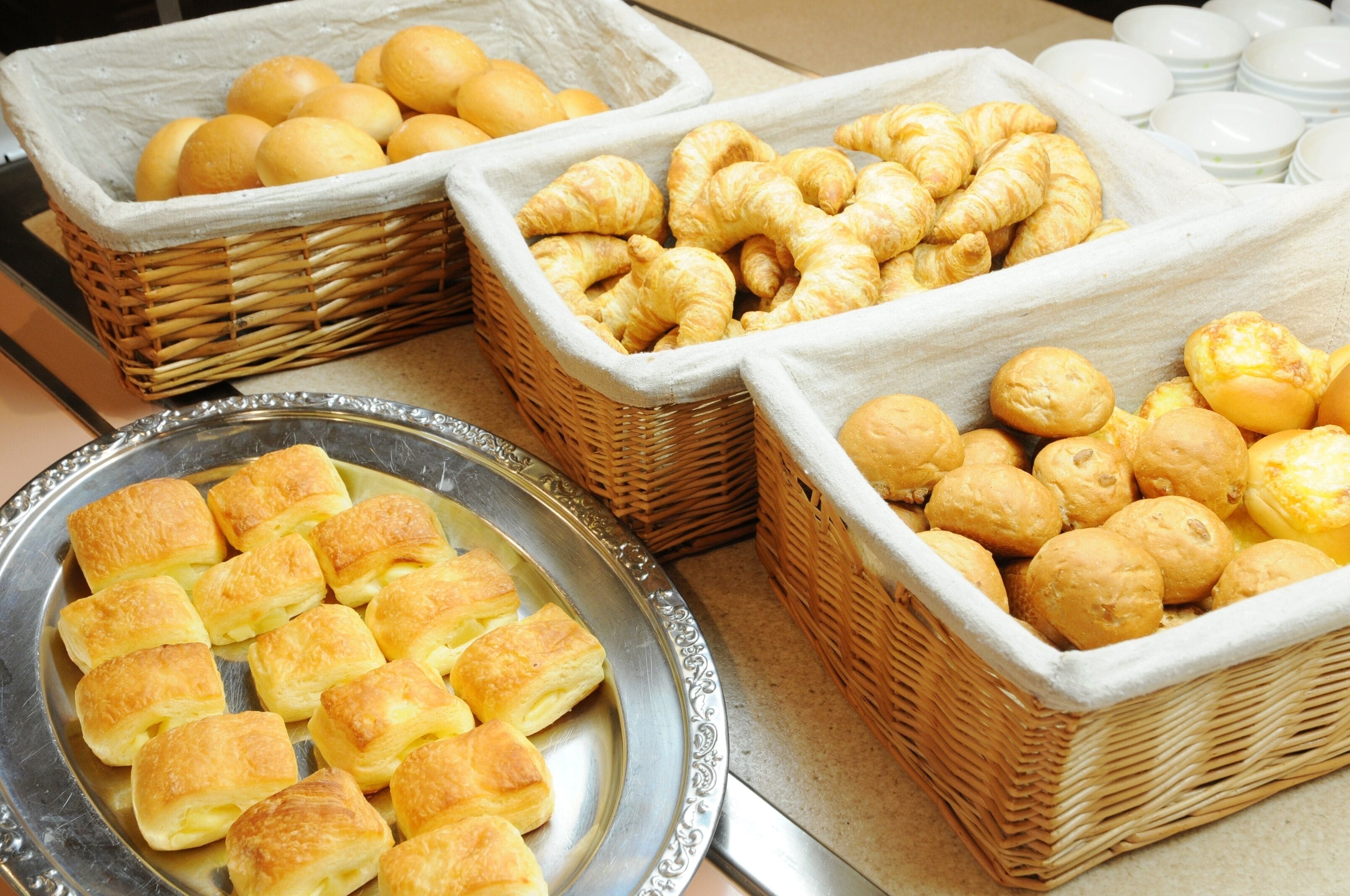 A buffet table with various baked goods including rolls, croissants, and puff pastries.