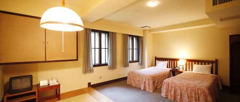 A hotel room with two beds, a television, a small table, and a traditional Japanese tatami mat floor.