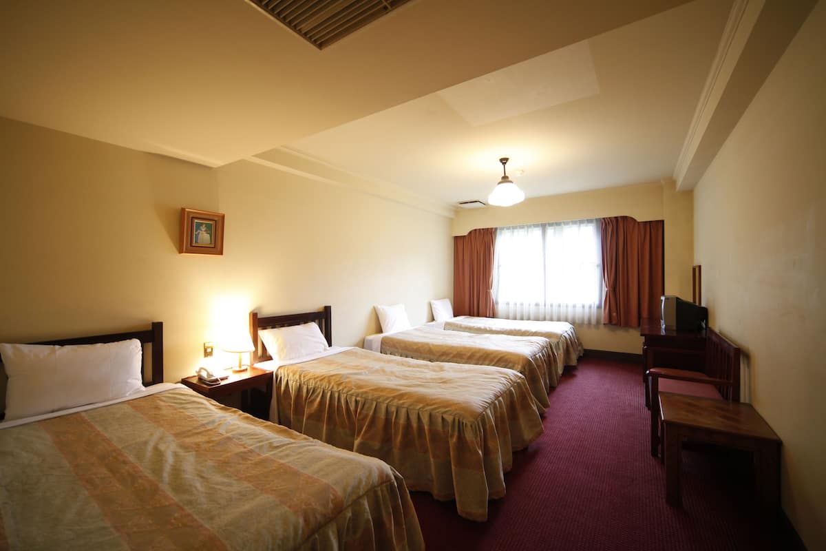 Quarto de hotel com quatro camas de solteiro, uma escrivaninha, uma cadeira e uma televisão.