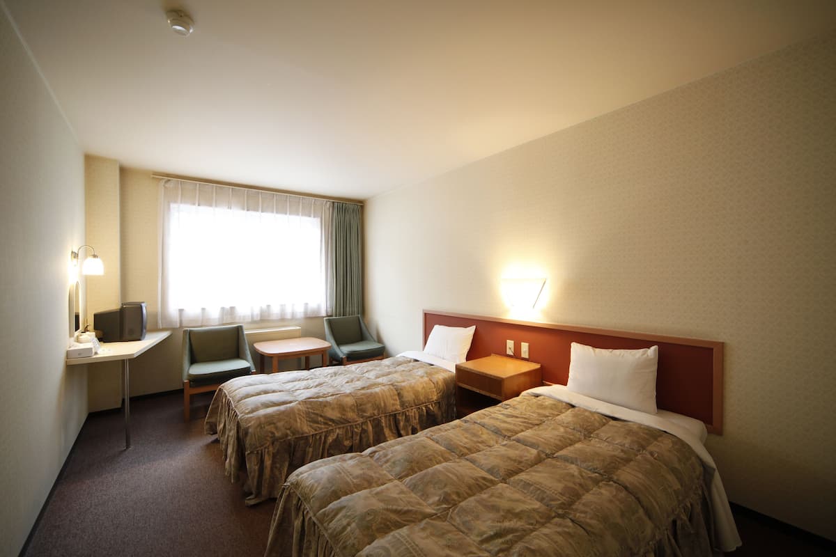 Quarto de hotel com duas camas, uma escrivaninha, uma cadeira e uma televisão.