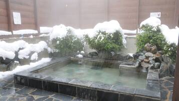 Un bain thermal en plein air, entouré de rochers et de buissons couverts de neige.