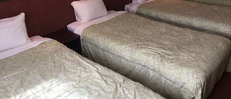 Une chambre d’hôtel avec trois lits simples, chacun agrémenté d’une couvre-lit à motifs et de coussins blancs.