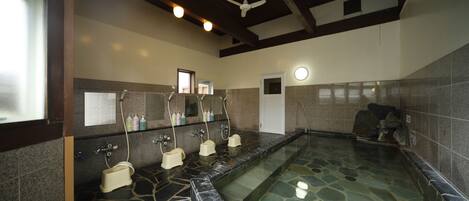 A public bath area with stone flooring, multiple sinks, and a ceiling fan.