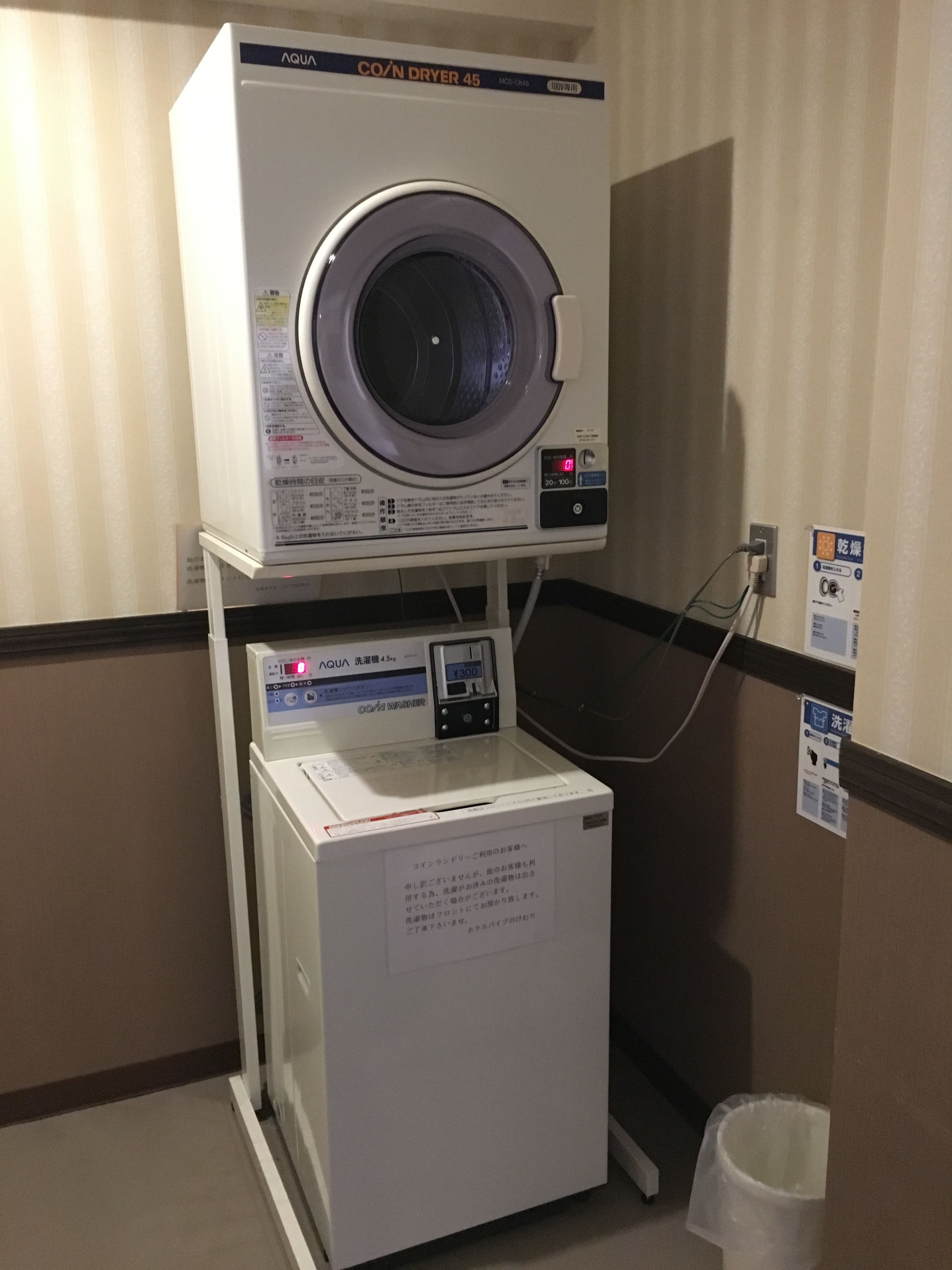 A coin dryer with a control panel and a washing machine below it.