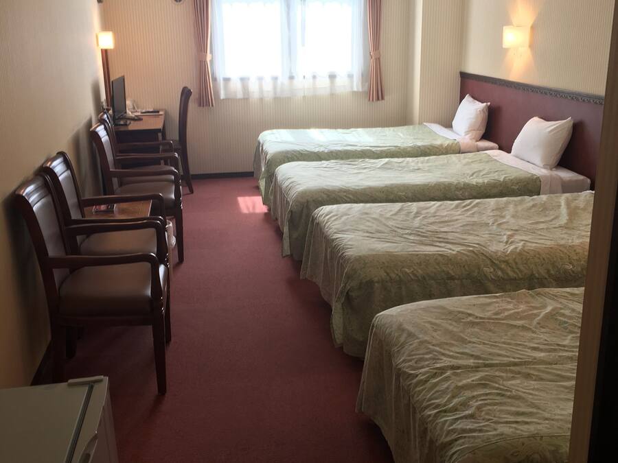 A hotel room with two beds, a desk, chairs, a refrigerator, and a window with curtains.