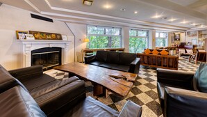 A spacious living area with a fireplace, leather sofas, a wooden coffee table, and large windows offering a view of greenery. - Hakuba PAIPU NO KEMURI (Hakuba)