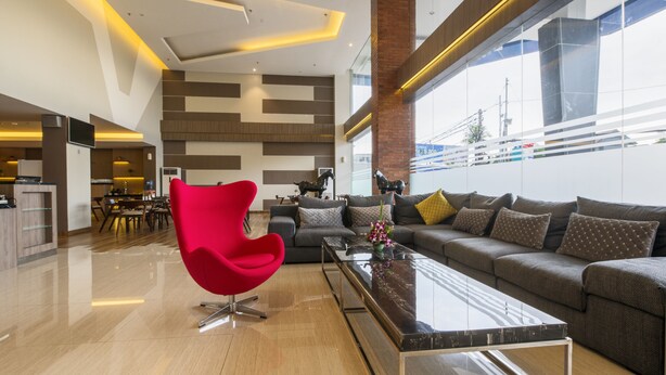 A modern living room with a red chair, a sofa, and a coffee table. There is a kitchen area in the background. - Hotel 88 Fatmawati Jakarta by WH (Jakarta)