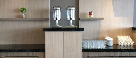 Una cocina moderna con armarios de madera, encimera negra y electrodomésticos de acero inoxidable. Se observan estantes con objetos decorativos, así como una variedad de cristalería y vajilla.