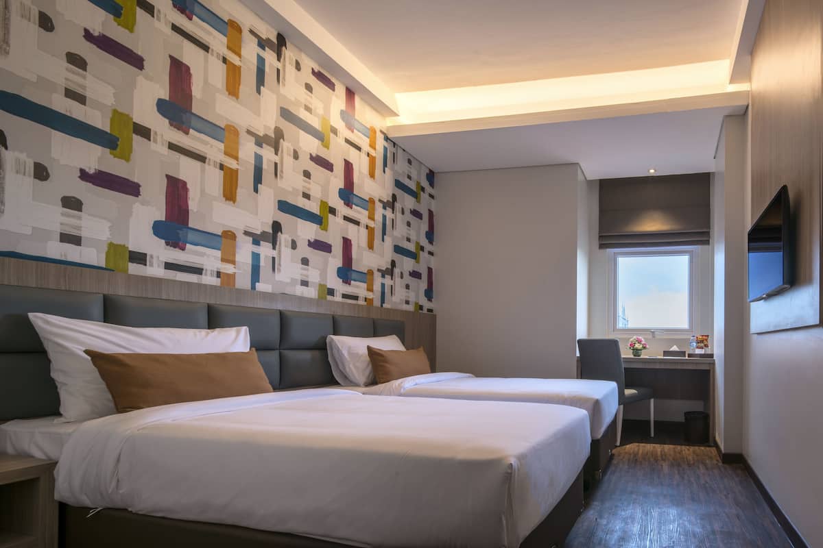 A hotel room with two beds, a desk, and a large abstract wall mural.