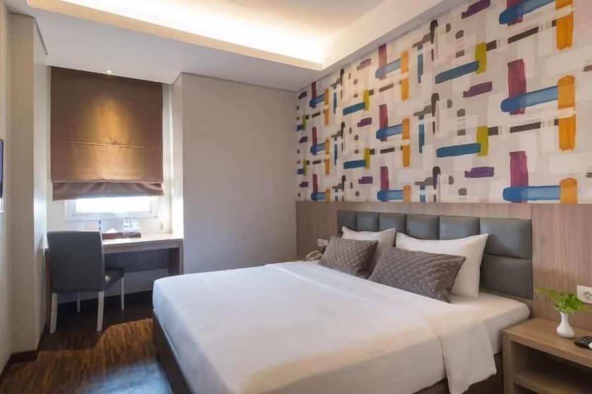 A hotel room with a bed, desk, chair, and a colorful abstract wall.