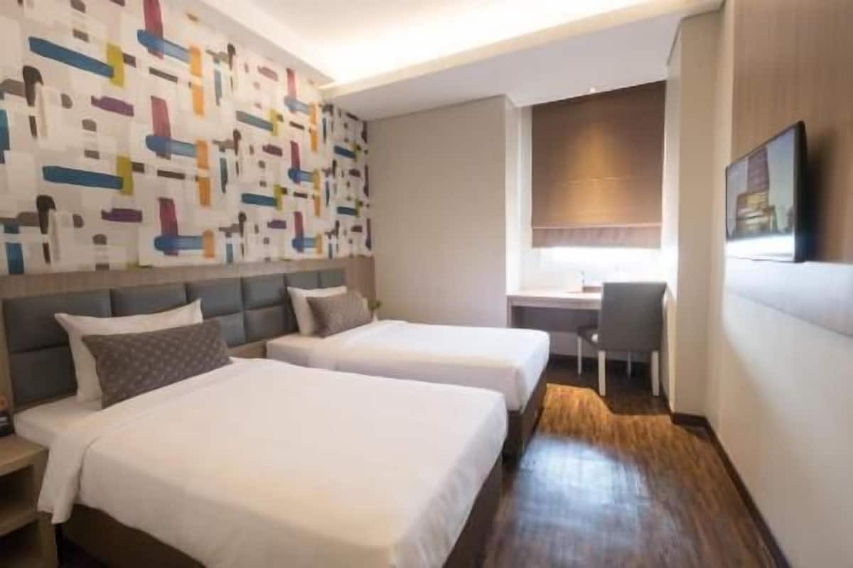 A hotel room with two beds, a desk, and a chair.