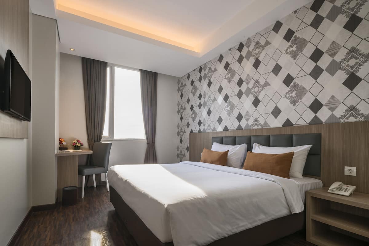 A hotel room with a large bed, a desk, a chair, a TV, and a patterned wall.