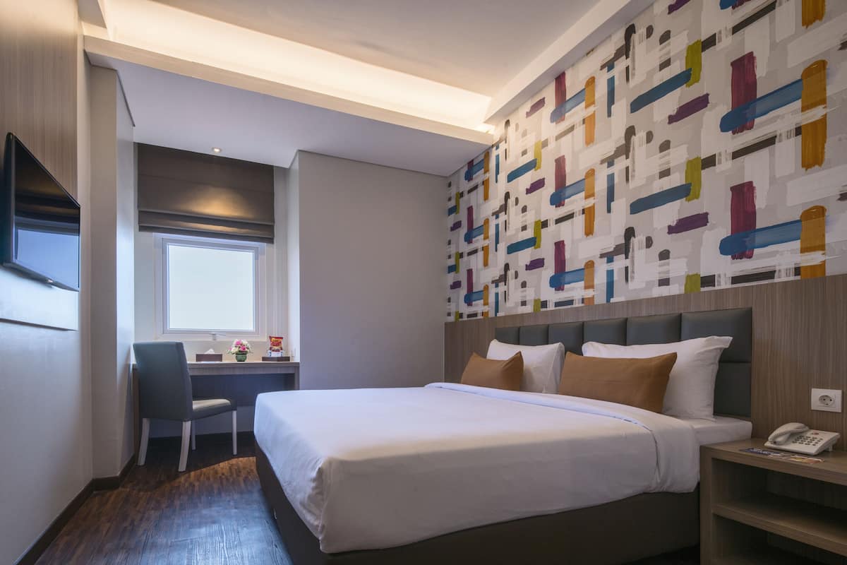 A hotel room with a large bed, a desk, and a chair.