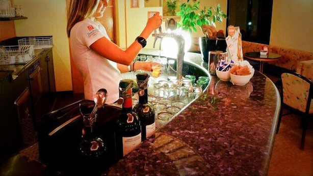 Un espace bar avec un barman préparant des boissons, un comptoir avec des bouteilles, des verres et un bol de collations.