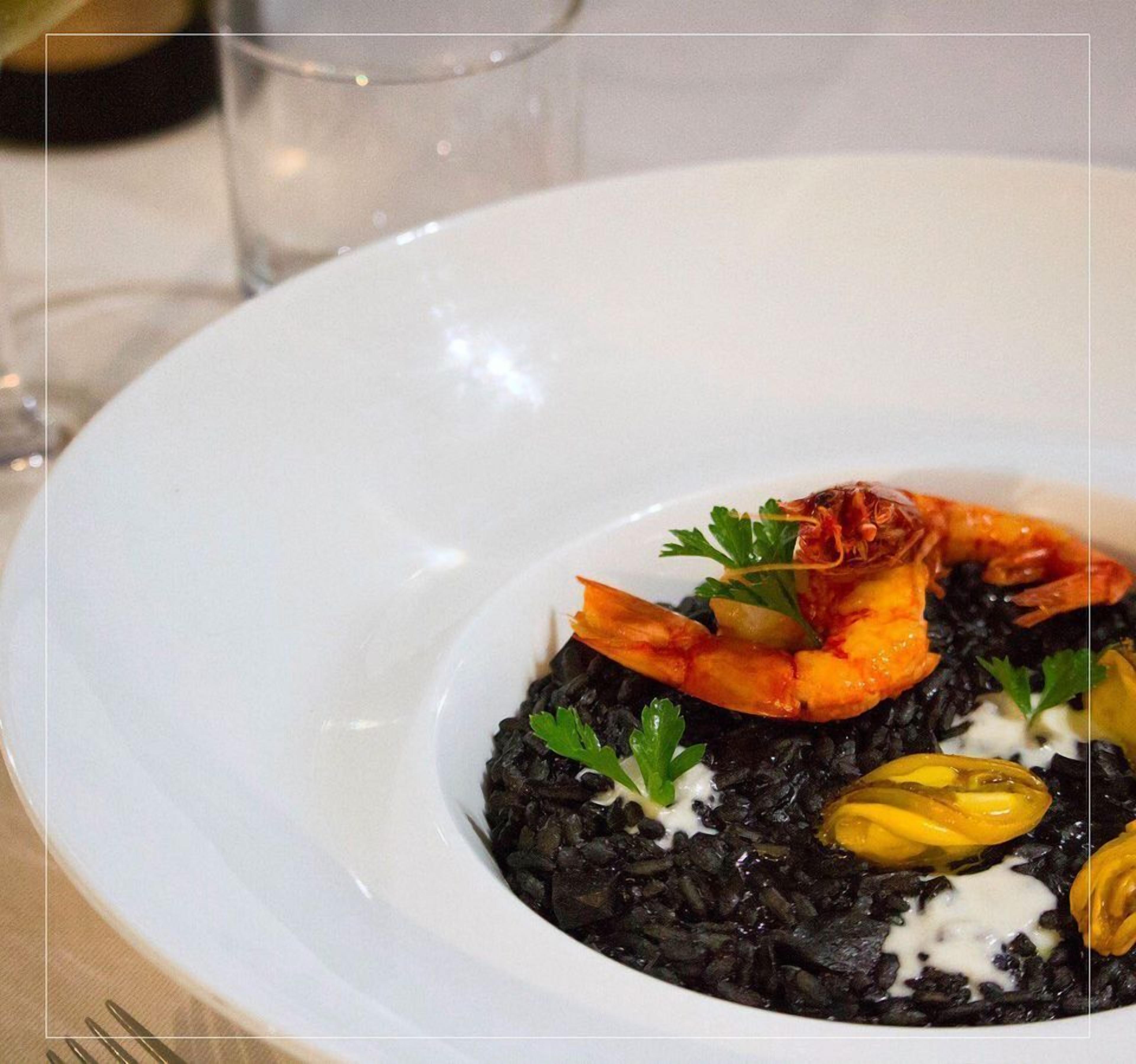 Une assiette blanche contenant un risotto noir, des crevettes et diverses garnitures.
