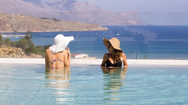 Dos personas en una piscina cristalina con vistas al mar y a las montañas.