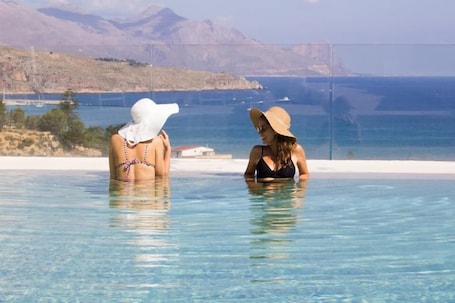 Two people in a clear pool with a view of the sea and mountains.