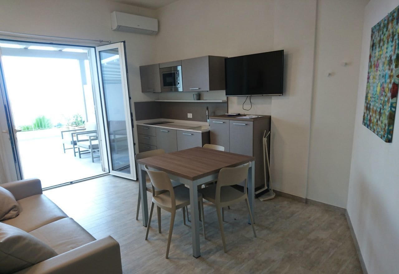 A compact kitchen with a microwave, a flat-screen TV, and a dining area with a table and chairs.