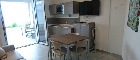 A compact kitchen with a microwave, a flat-screen TV, and a dining area with a table and chairs.