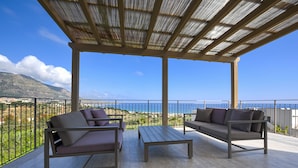 Un espacio al aire libre techado con dos sofás y una mesa, con vistas panorámicas al mar y las montañas.