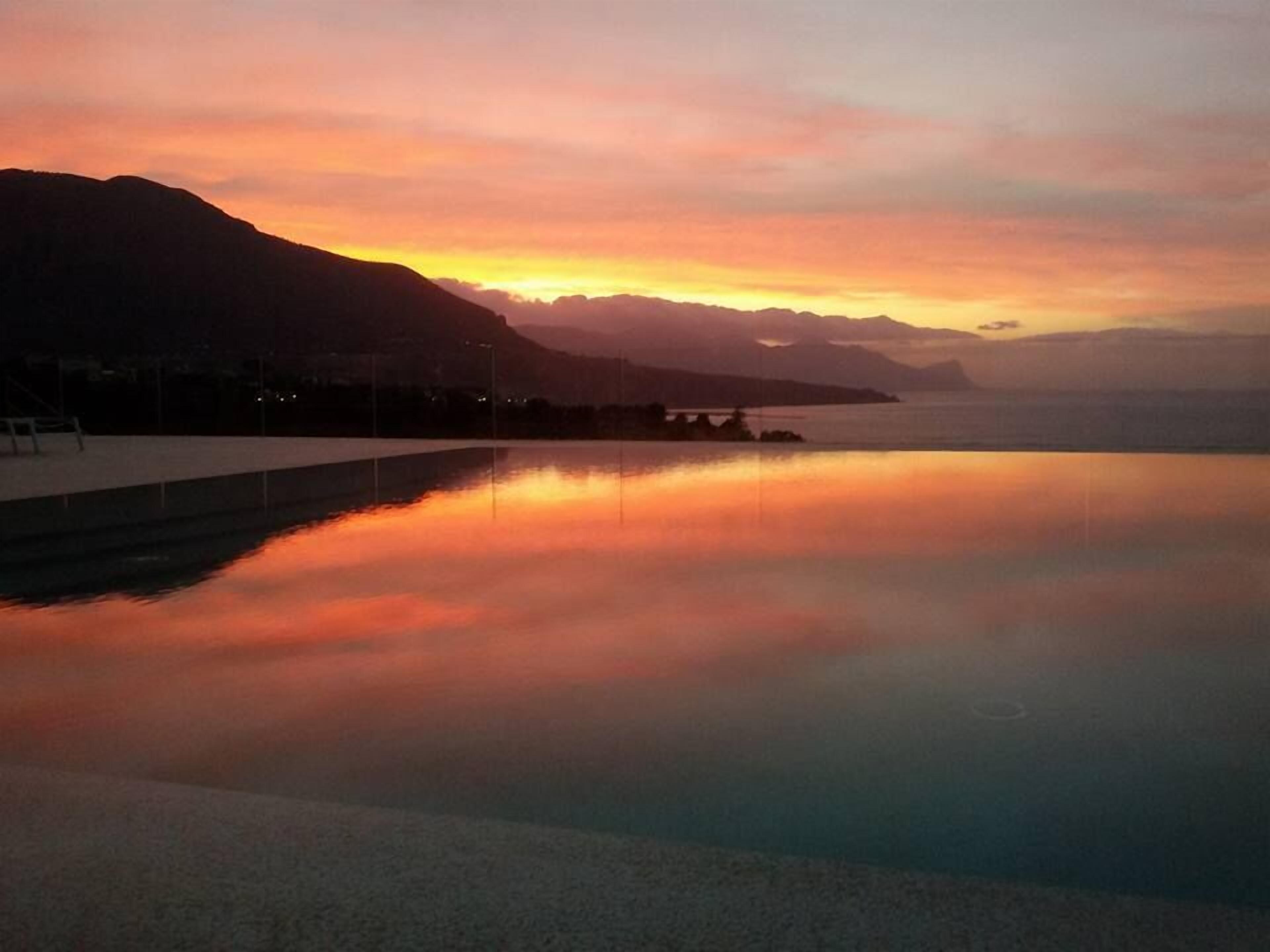 A calm body of water reflecting a sunset with mountains in the background.