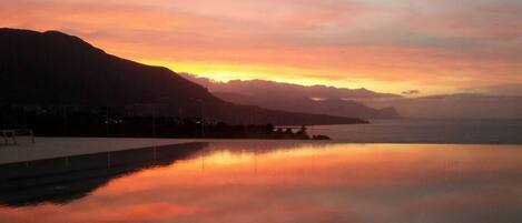 A calm body of water reflecting a sunset with mountains in the background.