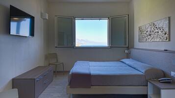 A bedroom with a bed, a desk, a chair, a TV, and a window with a view.
