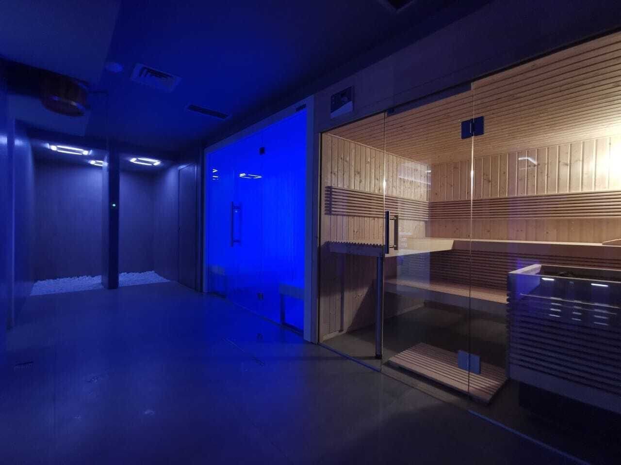 A modern interior with a glass door entrance, a wooden panel wall, and a blue-lit corridor.