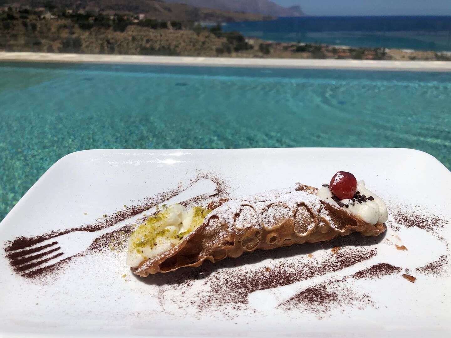 Un dessert servi dans une assiette blanche, avec en arrière-plan une vue panoramique sur une plage.