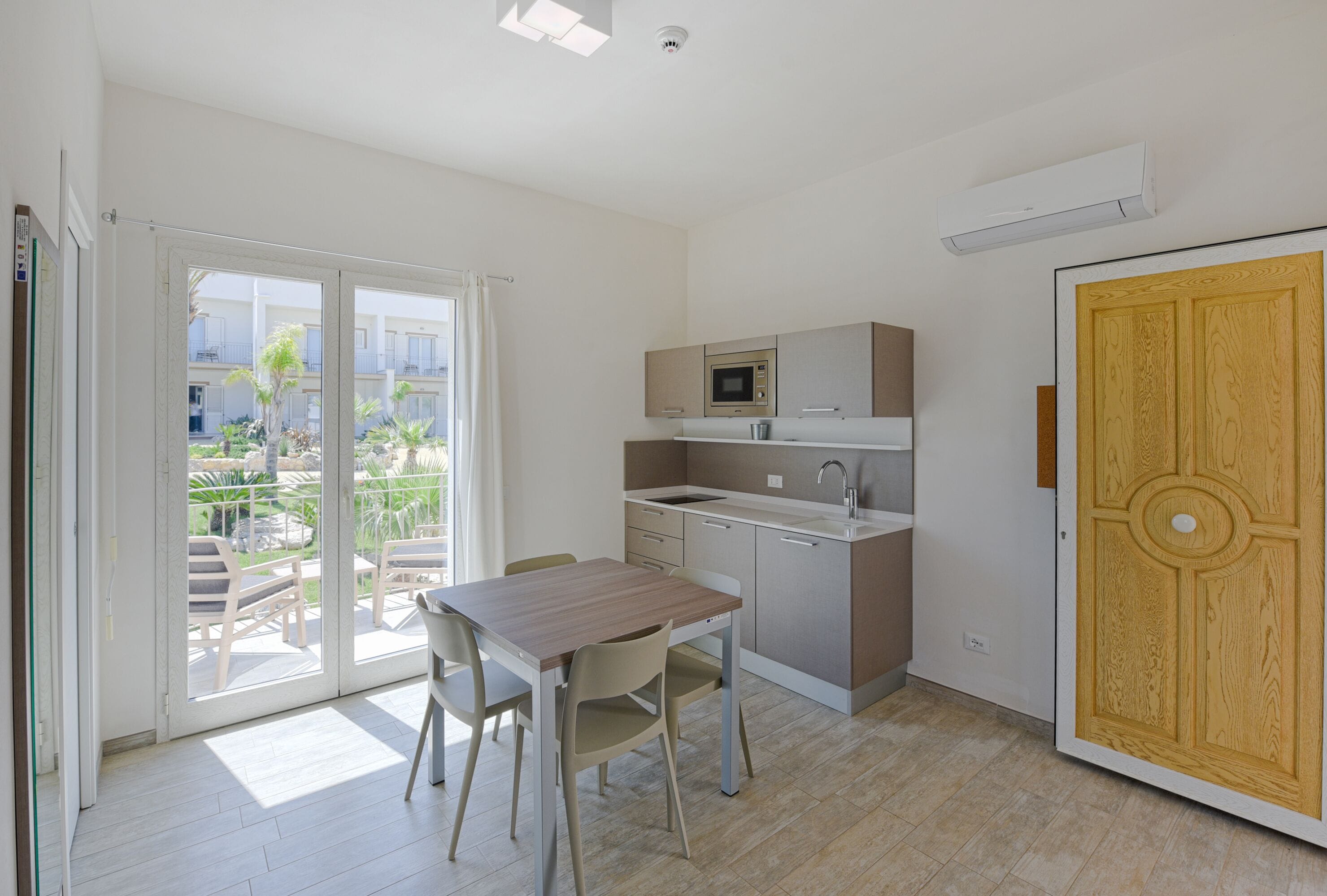 Una cucina compatta con angolo ristoro, una porta scorrevole in vetro su un balcone e una porta in legno.