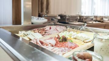 A buffet with various meats, cheeses, and a jar of yogurt parfait.