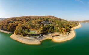 A large, multi-story building surrounded by dense forest on a hilly island. - Domaša Zelená Lagúna (Kvakovce)
