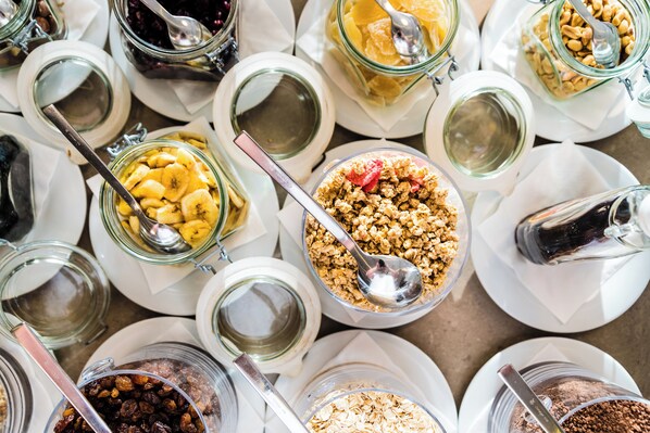 Variedad de alimentos en recipientes de vidrio sobre platos blancos, como nueces, frutas secas y granola.