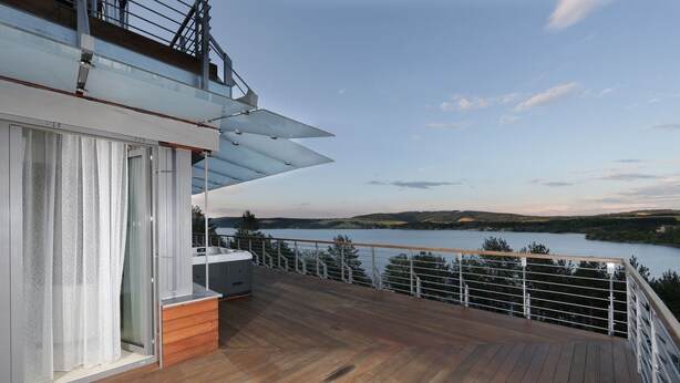 A wooden deck with a glass door leading to a room, overlooking a lake and hills. - Domaša Zelená Lagúna (Kvakovce)