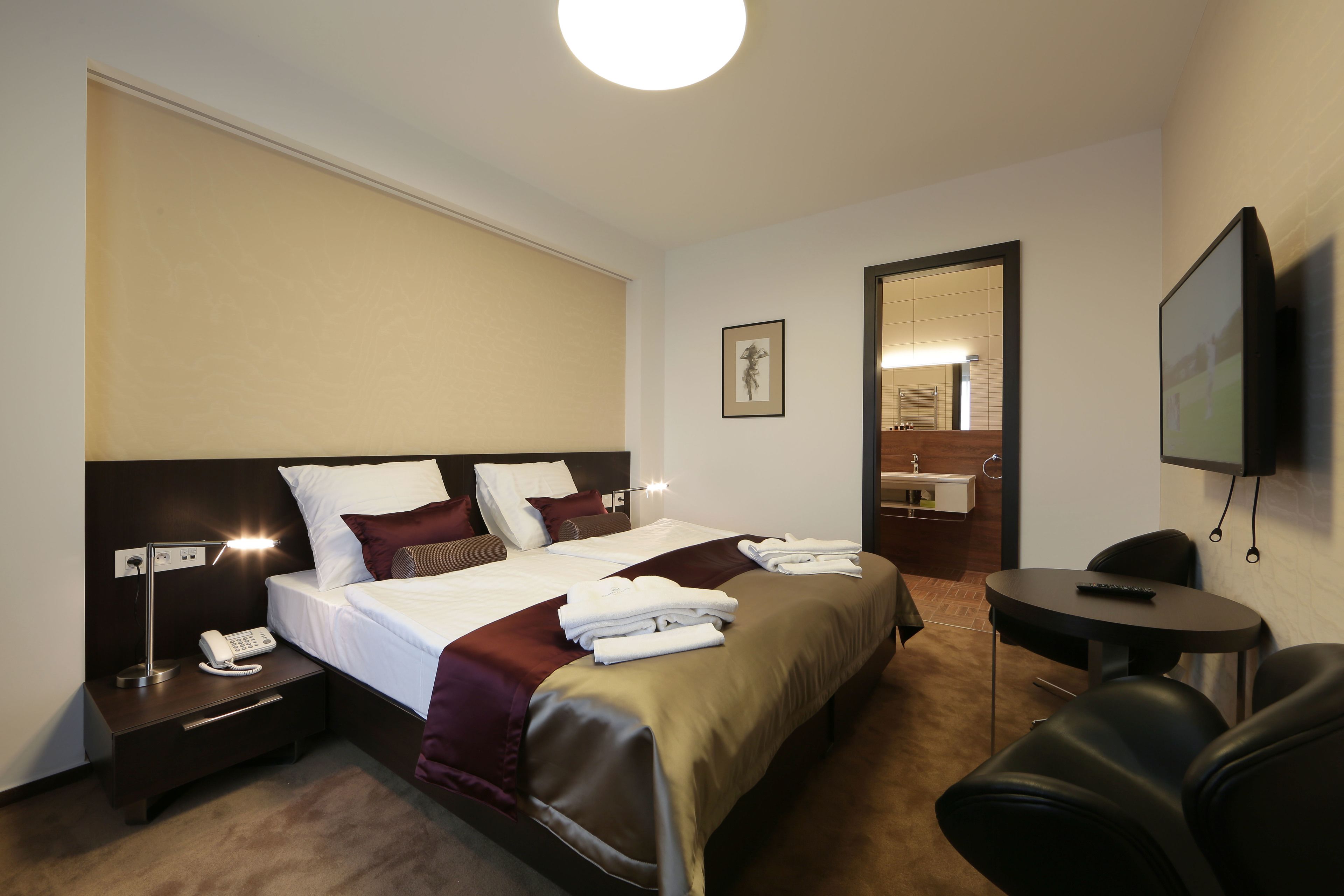 Une chambre d’hôtel avec un grand lit, des tables de chevet avec des lampes, une télévision et une petite table avec des chaises.