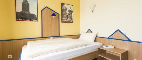 A single-bed room with a wooden headboard, a small bedside table, and two framed pictures on the wall.