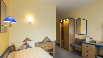 A hotel room with a bed, bedside table, lamp, wardrobe, mirror, and a desk with a telephone.
