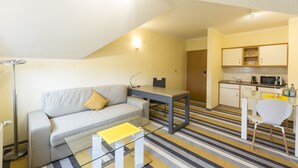 A compact living space with a sofa, a glass coffee table, a kitchenette, and a striped floor. - Hotel Globotel Business (Garbsen)