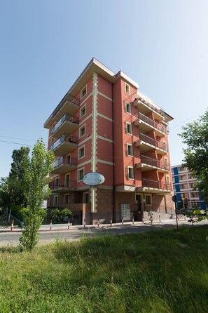 Un edificio de varios pisos con balcones, un cartel que indica 'Hotel Mamaia Luxury Homes' y una zona verde al frente.