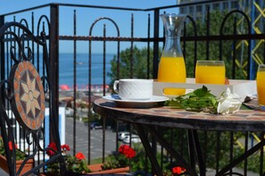 Una mesa con una taza blanca, una jarra de vidrio y dos vasos de jugo de naranja, frente a una vista panorámica del mar.