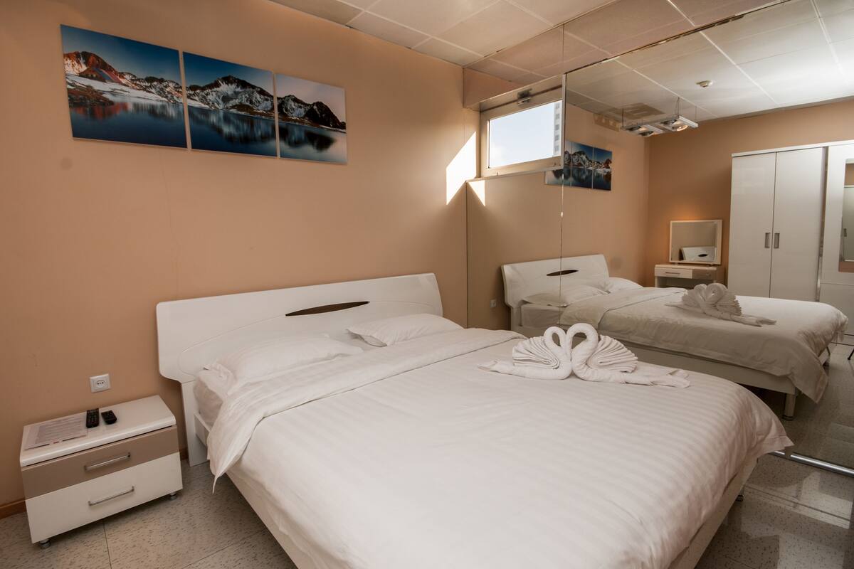 A hotel room with two beds, a nightstand, a dresser, a mirror, and artwork on the wall.