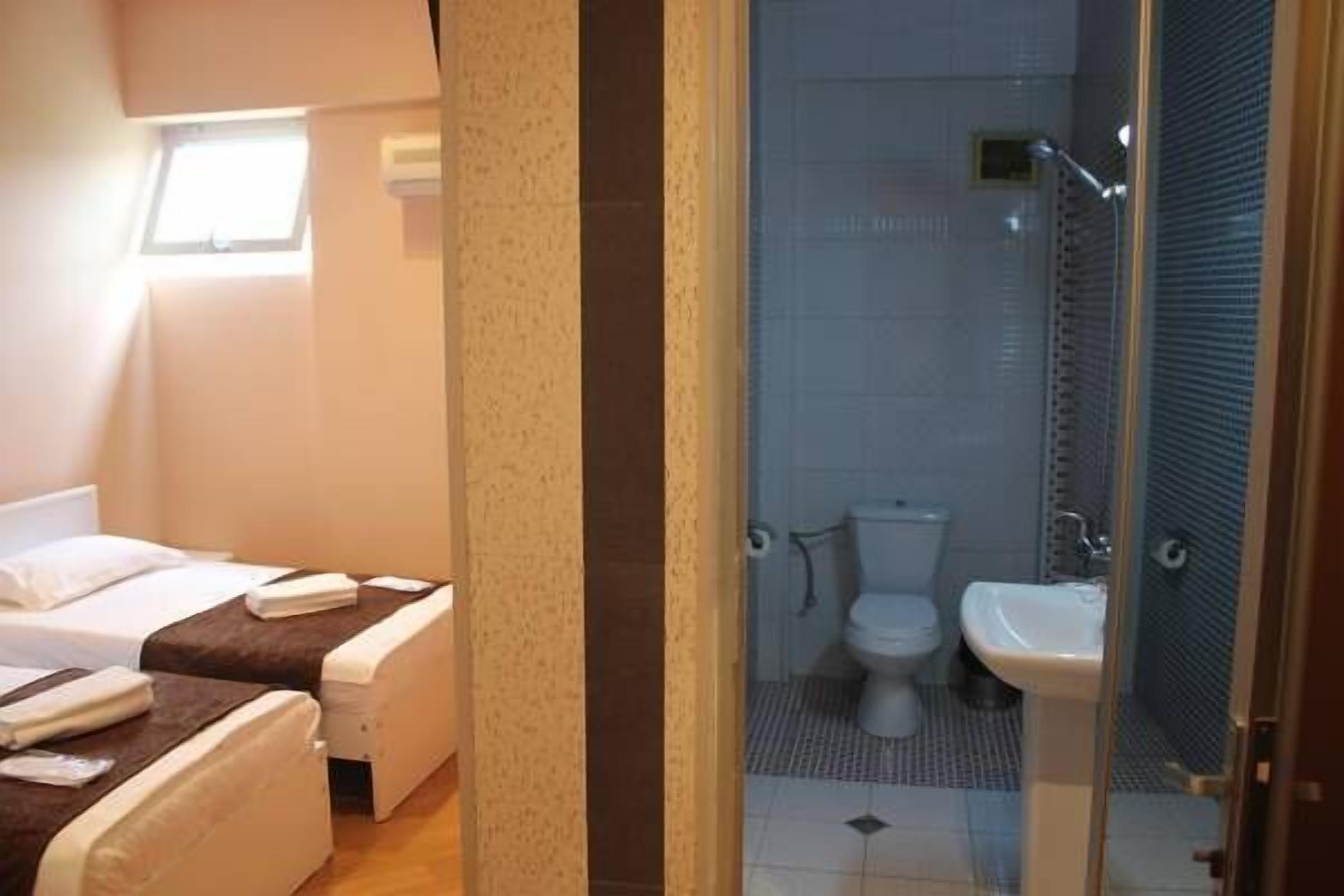 Habitación de hotel con dos camas, baño con ducha y un ventanal pequeño.