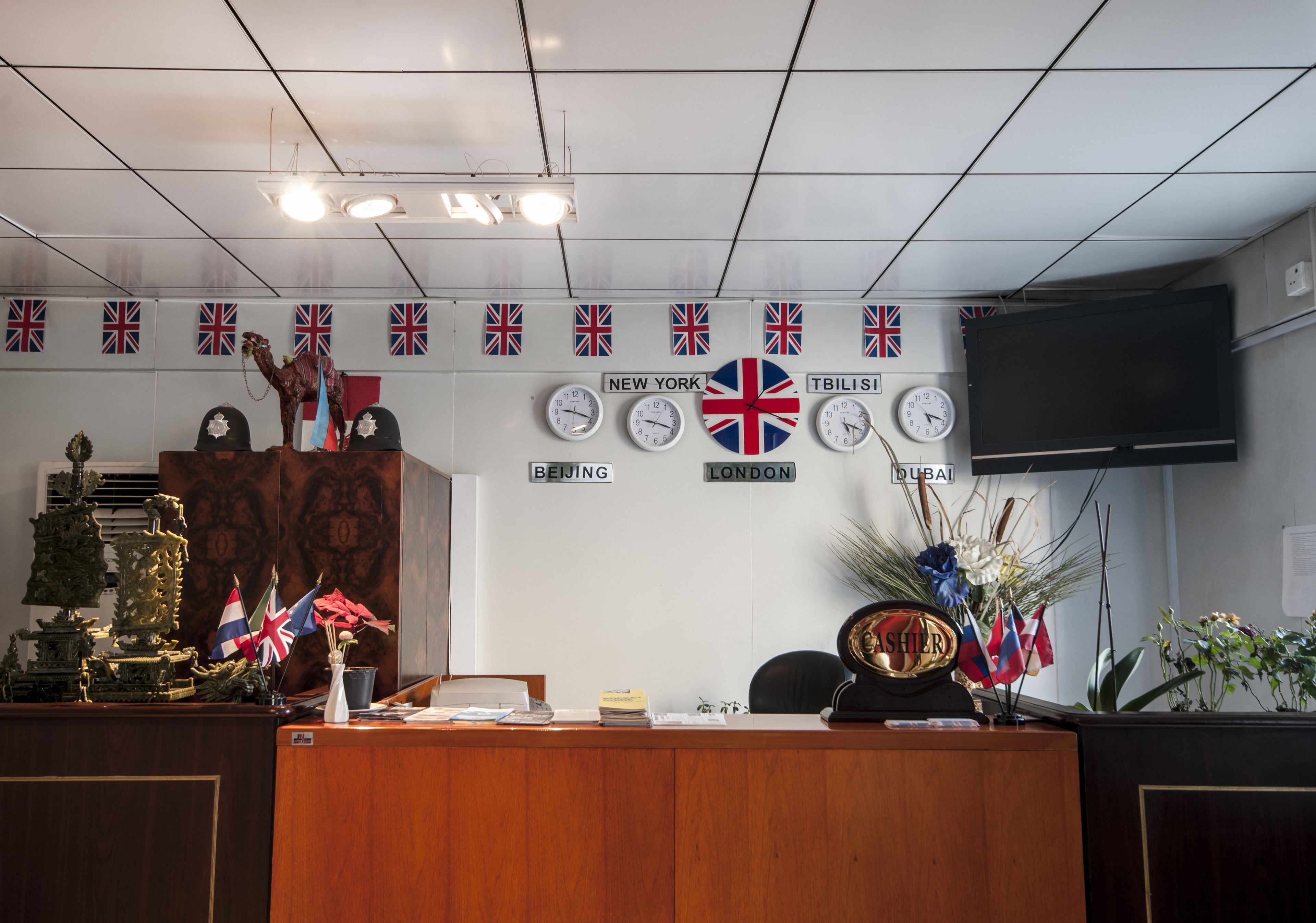 Et kontor med et træbord, flere ure, flag og et fjernsyn monteret på væggen.