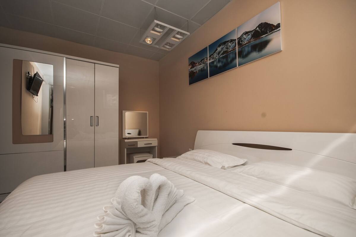 A hotel room with a bed, a wardrobe, a desk, and a wall-mounted artwork.